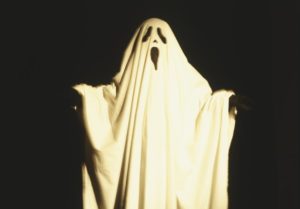 Child dressed up as ghost draped with white sheet that has facial features cut out, extending arms to the sides, front view.